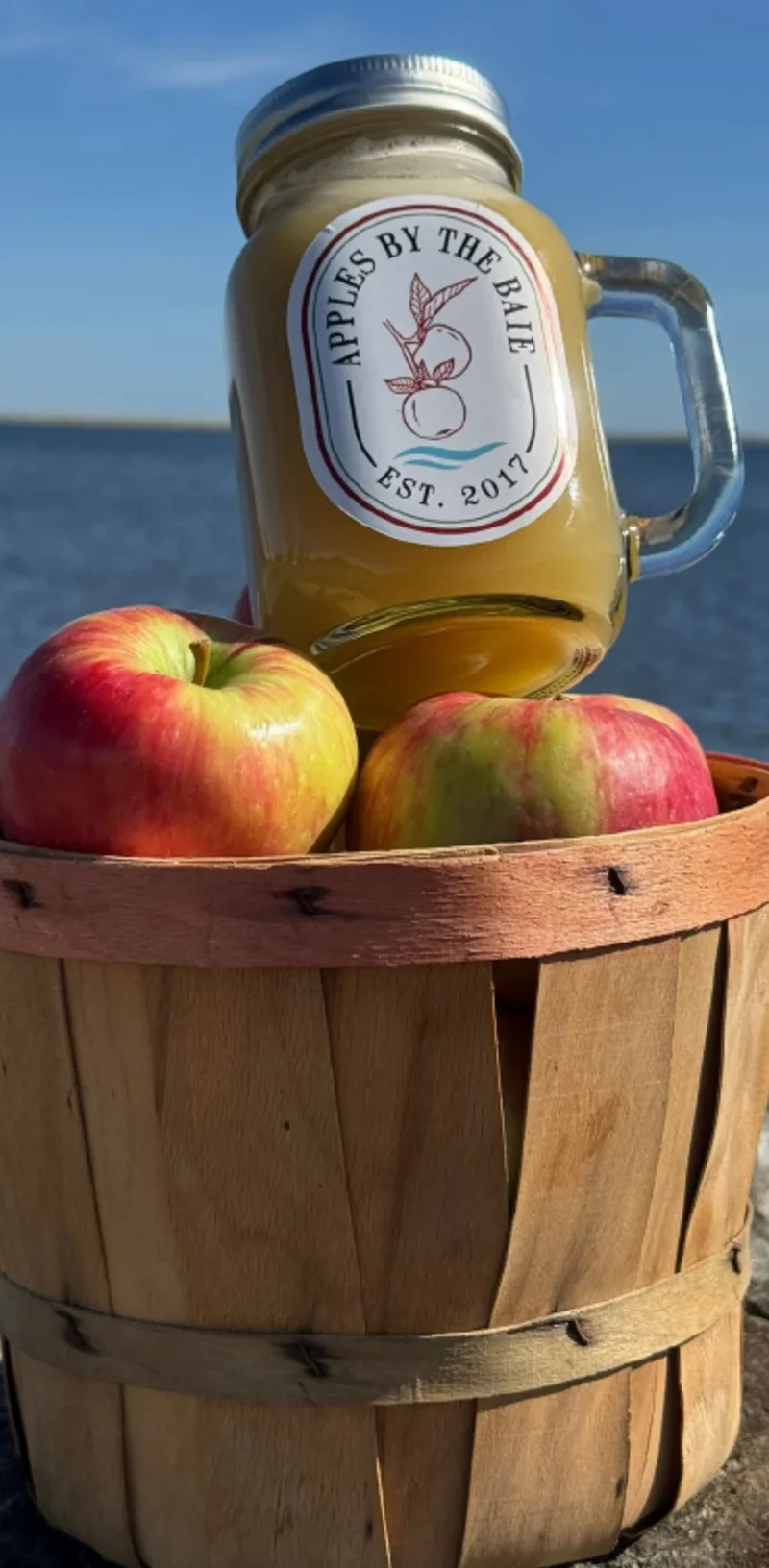 Jar of orchard juice beside apples in a wooden basket